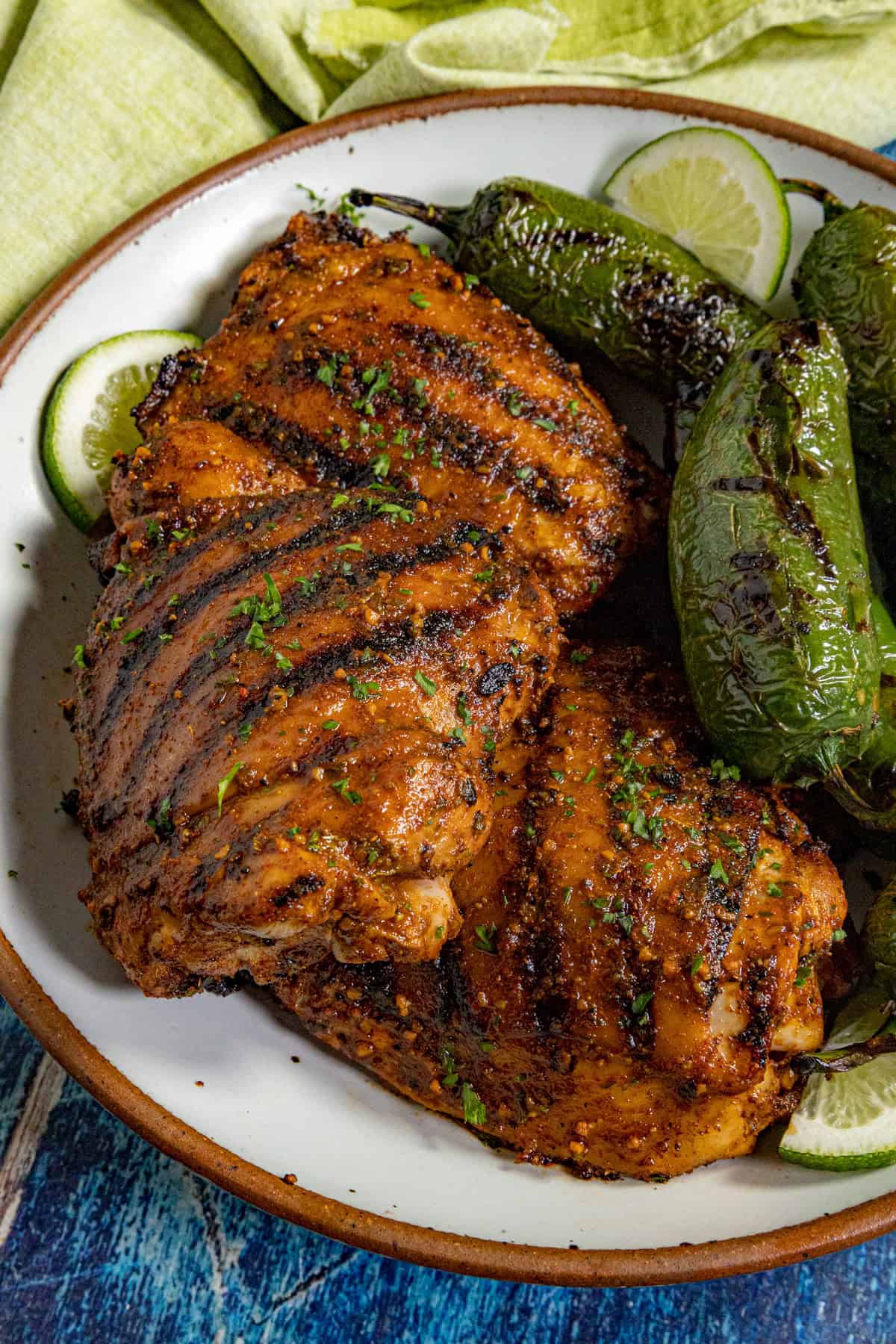 Grilled chicken thighs, marinated in a zesty Mexican Chicken Marinade, display char marks and are garnished with herbs, served alongside grilled jalapeño peppers and lime slices.