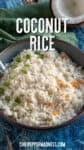 A bowl of Coconut Rice garnished with chopped green onions and small orange pepper pieces sits on a blue surface, accompanied by a green napkin and half a coconut in the background. Text reads Coconut Rice.