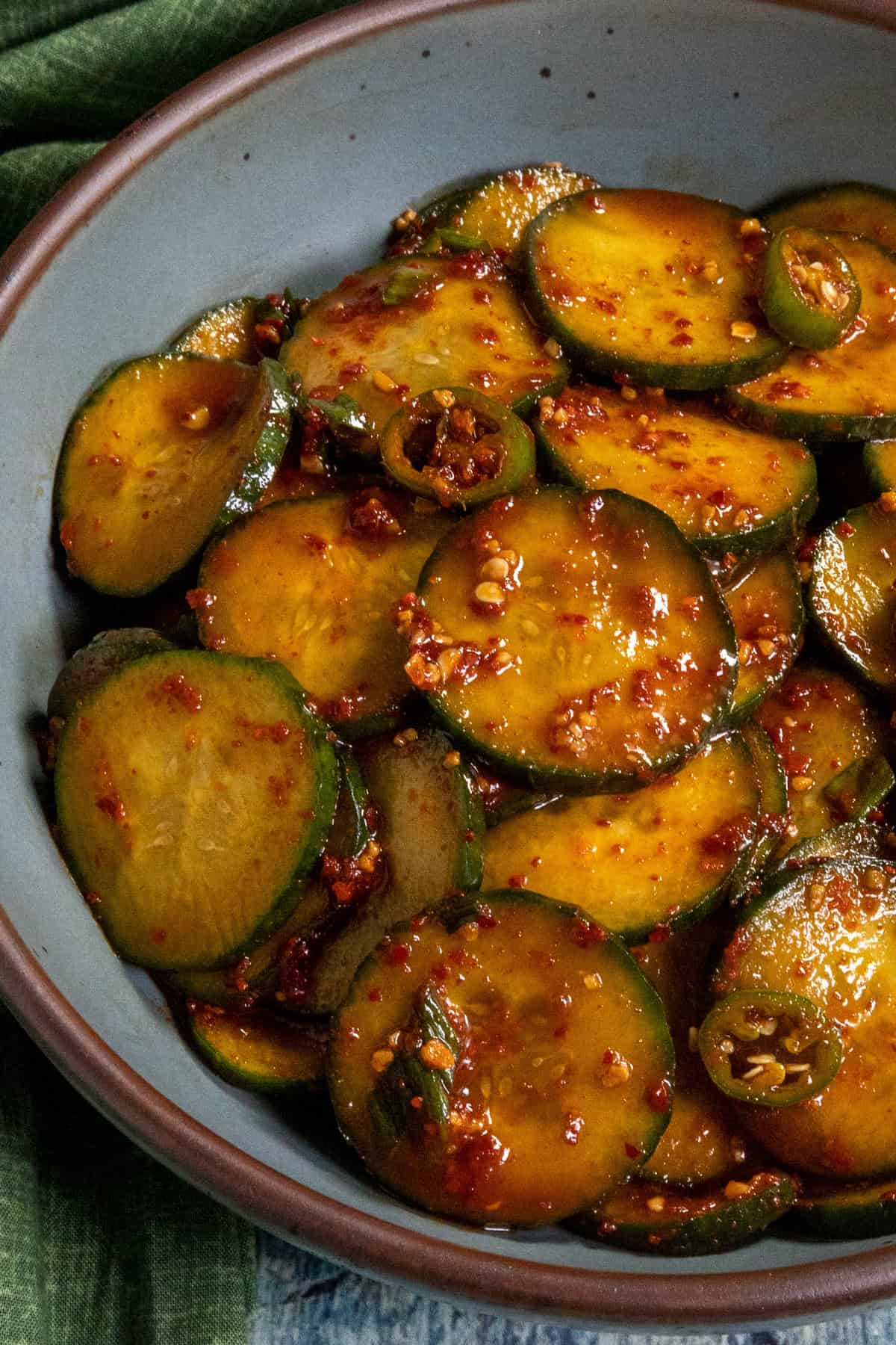 A bowl filled with sliced cucumbers coated in a spicy red chili sauce, garnished with crushed red pepper and herbs—this vibrant Korean Cucumber Salad offers a refreshing, zesty bite.