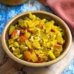 A brown bowl filled with colorful diced vegetables, including yellow, green, and red pieces—likely Chow Chow Relish—sits on a wooden board with a blue and red background.