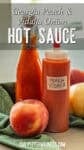 Two bottles of Georgia Peach Vidalia Onion Hot Sauce rest on a green cloth, flanked by a fresh peach and a Vidalia onion. Above them, the label proudly announces this flavorful Southern blend.