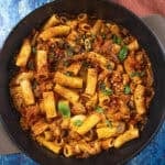 A black skillet filled with Chicken Riggies—rigatoni pasta in a tomato-based sauce with vegetables and tender pieces of chicken, garnished with fresh basil leaves.