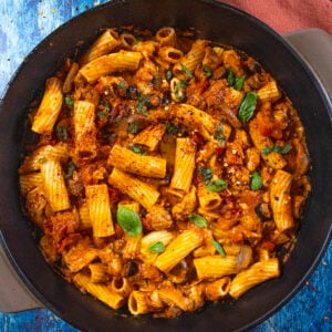 A black skillet filled with Chicken Riggies—rigatoni pasta in a tomato-based sauce with vegetables and tender pieces of chicken, garnished with fresh basil leaves.