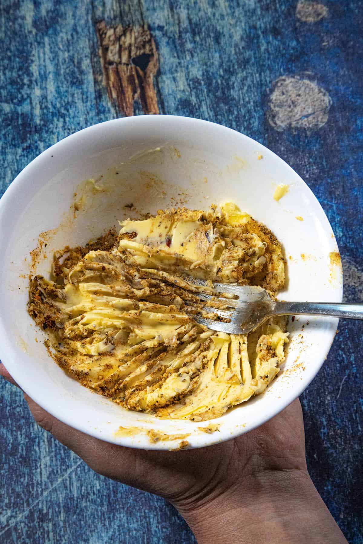 Mike from Chili Pepper Madness using a fork to mix cowboy butter seasoning into a white bowl filled with butter for easy cowboy butter