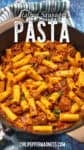A skillet filled with hearty Italian Sausage Pasta—rigatoni tossed with savory Italian sausage, tomato sauce, and fragrant herbs. The dish is topped with red pepper flakes and set on a blue wooden surface with a striped cloth nearby. Text reads Italian Sausage Pasta.