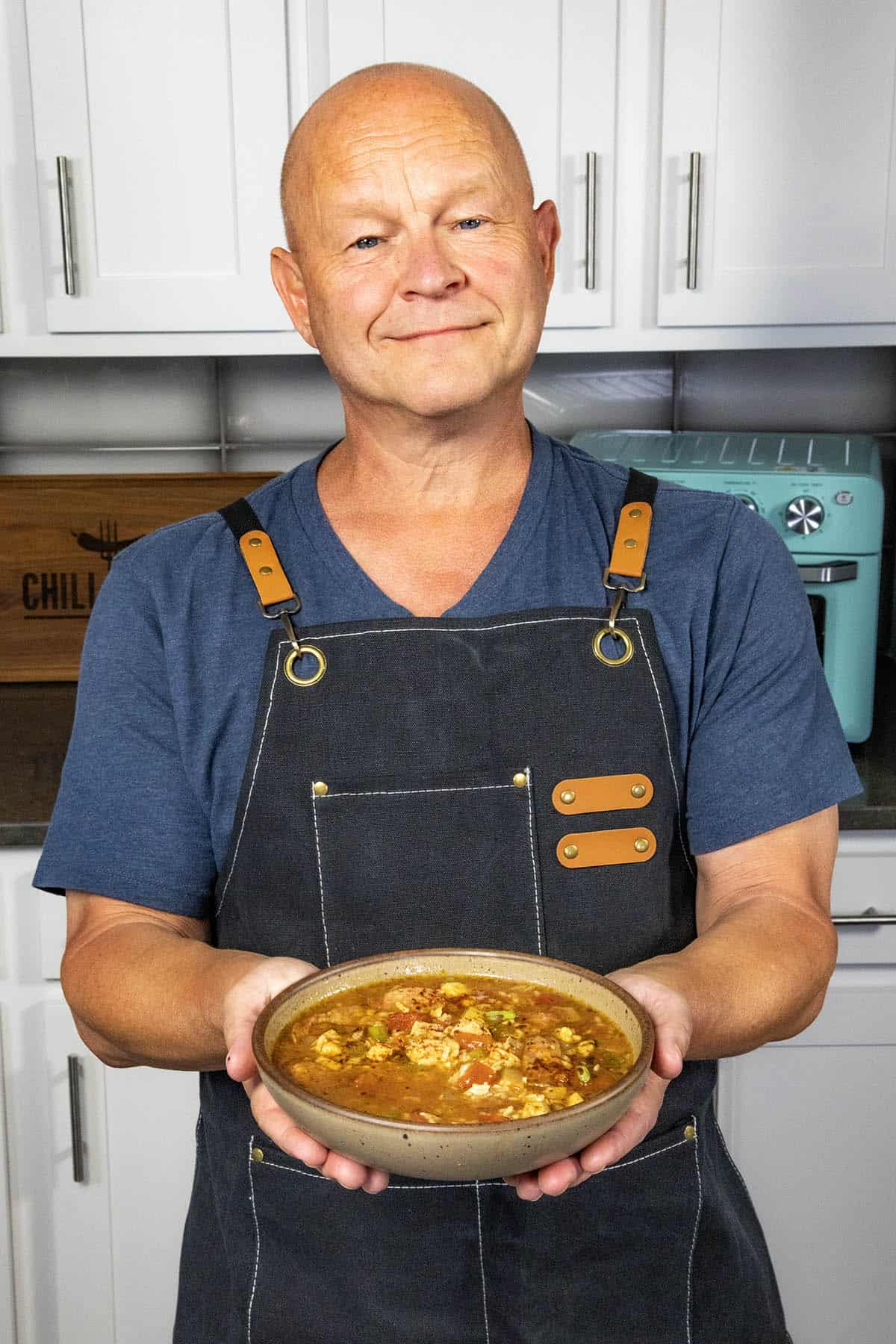 Mike Hultquist from Chili Pepper Madness holding a hearty bowl of jambalaya soup with a big smile on his face