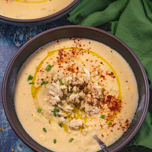 Two bowls of creamy She Crab Soup served with extra crab meat over the top, drizzled with olive oil, dusted with bright red paprika and sprinkled with fresh chopped chives