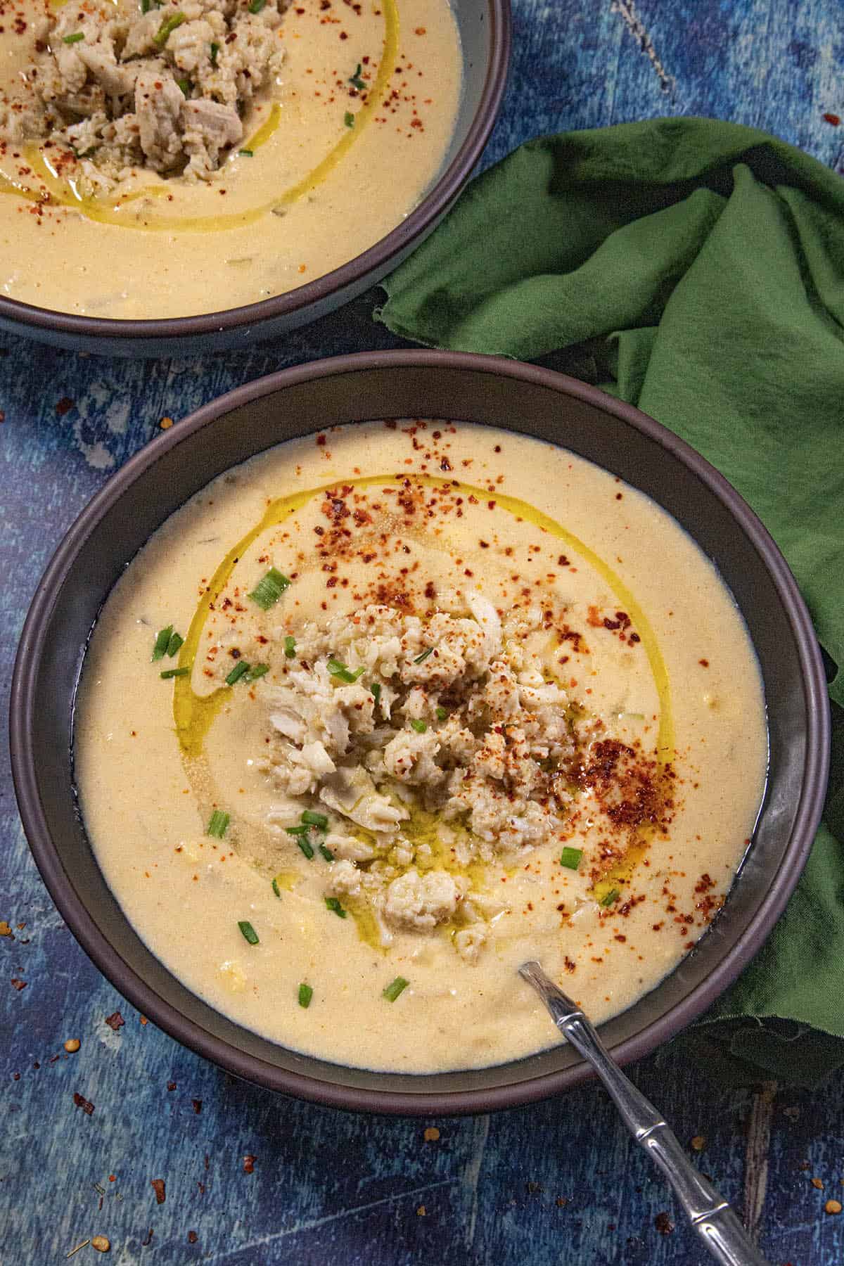 Two bowls of creamy She Crab Soup served with extra crab meat over the top, drizzled with olive oil, dusted with bright red paprika and sprinkled with fresh chopped chives