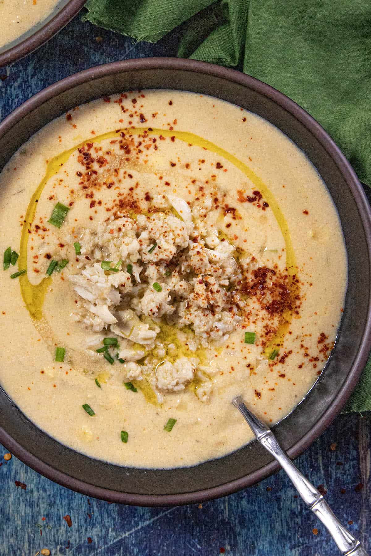Creamy She Crab Soup served in a bowl with a spoon, topped with a mound of fresh crab meat, garnished with paprika, olive oil drizzle, and fresh chopped chives