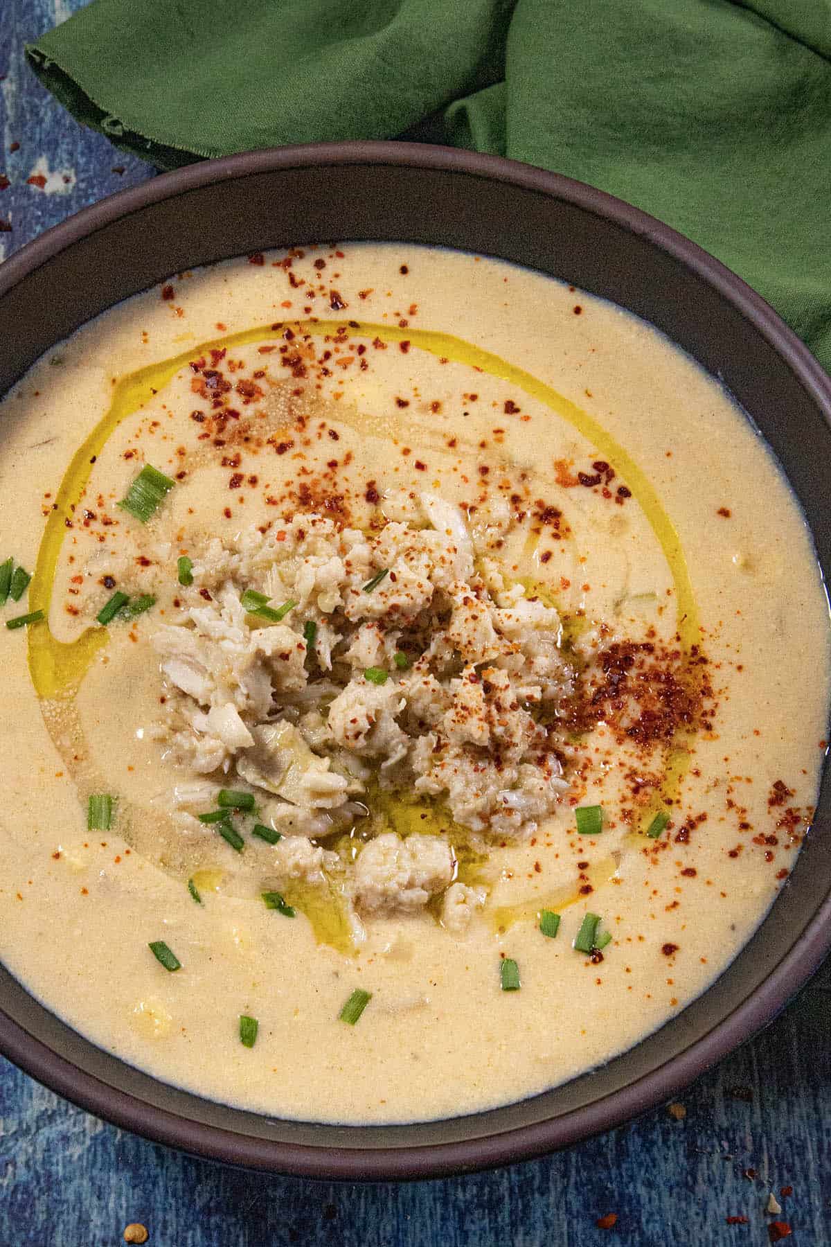 A large bowl of creamy She Crab Soup, topped with crab meat, garnished with paprika, olive oil drizzle, and fresh chopped chives