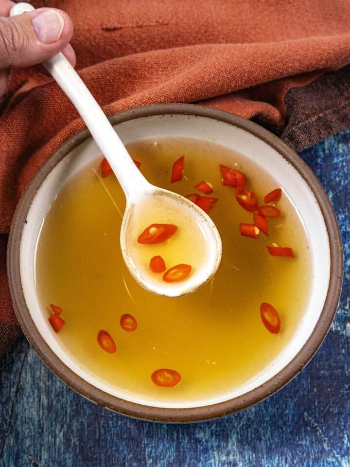 Mike from Chili Pepper Madness scooping golden Nuoc Cham (Vietnamese Dipping Sauce) from a bowl with a white spoon