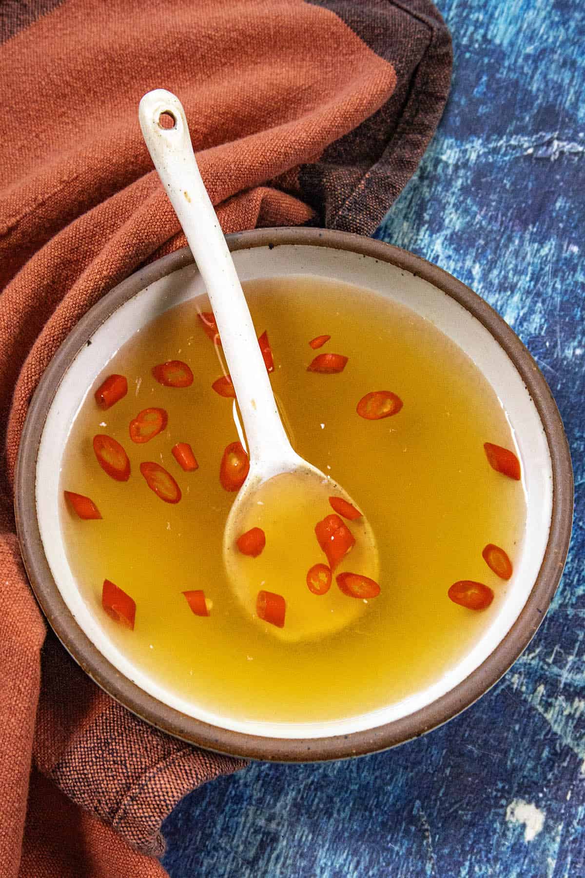 A small bowl of amber colored Nuoc Cham (Vietnamese Dipping Sauce), with sliced red chili peppers and a white spoon, ready for dipping.