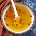 A small bowl of nuoc cham Vietnamese dipping sauce with floating garlic and sliced Thai chilies, with limes on the side