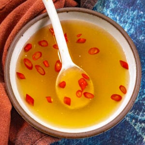 A small bowl of nuoc cham Vietnamese dipping sauce with floating garlic and sliced Thai chilies, with limes on the side