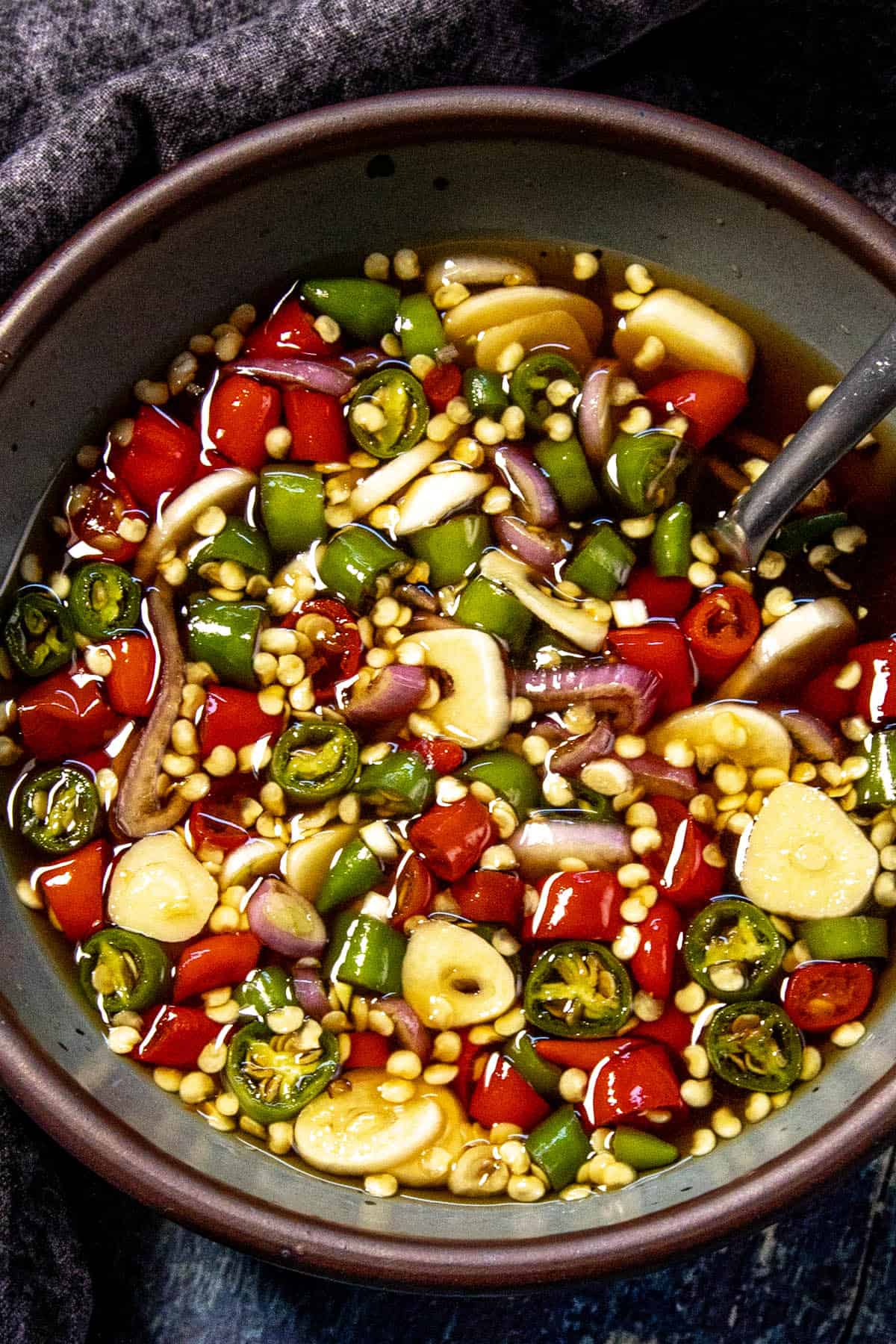 A bowl filled with sliced green and red chili peppers, garlic, and shallots in fish sauce with a spoon inside—this vibrant mix is perfect for making Prik Nam Pla (Authentic Thai Dipping Sauce).
