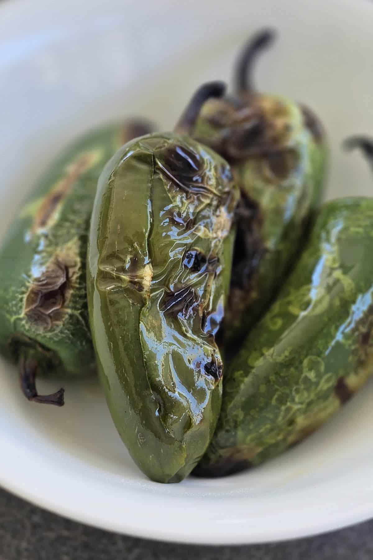 Three roasted jalapeño peppers with charred, blistered skins sit on a white plate.