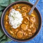 A bowl of rich Cajun Chicken and Sausage Gumbo with sliced sausage, chunks of meat, and vegetables is served with a mound of white rice on top.