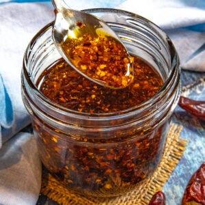 A spoonful of Calabrian Chili Oil (Olio Santo) filled with chili flakes being lifted from a jar