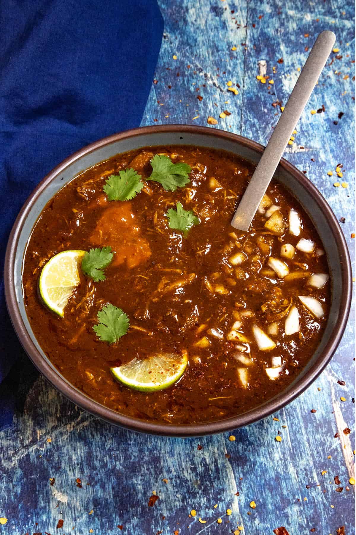 A bowl of Chicken Birria (Birria de Pollo) garnished with fresh lime, white onion, and cilantro