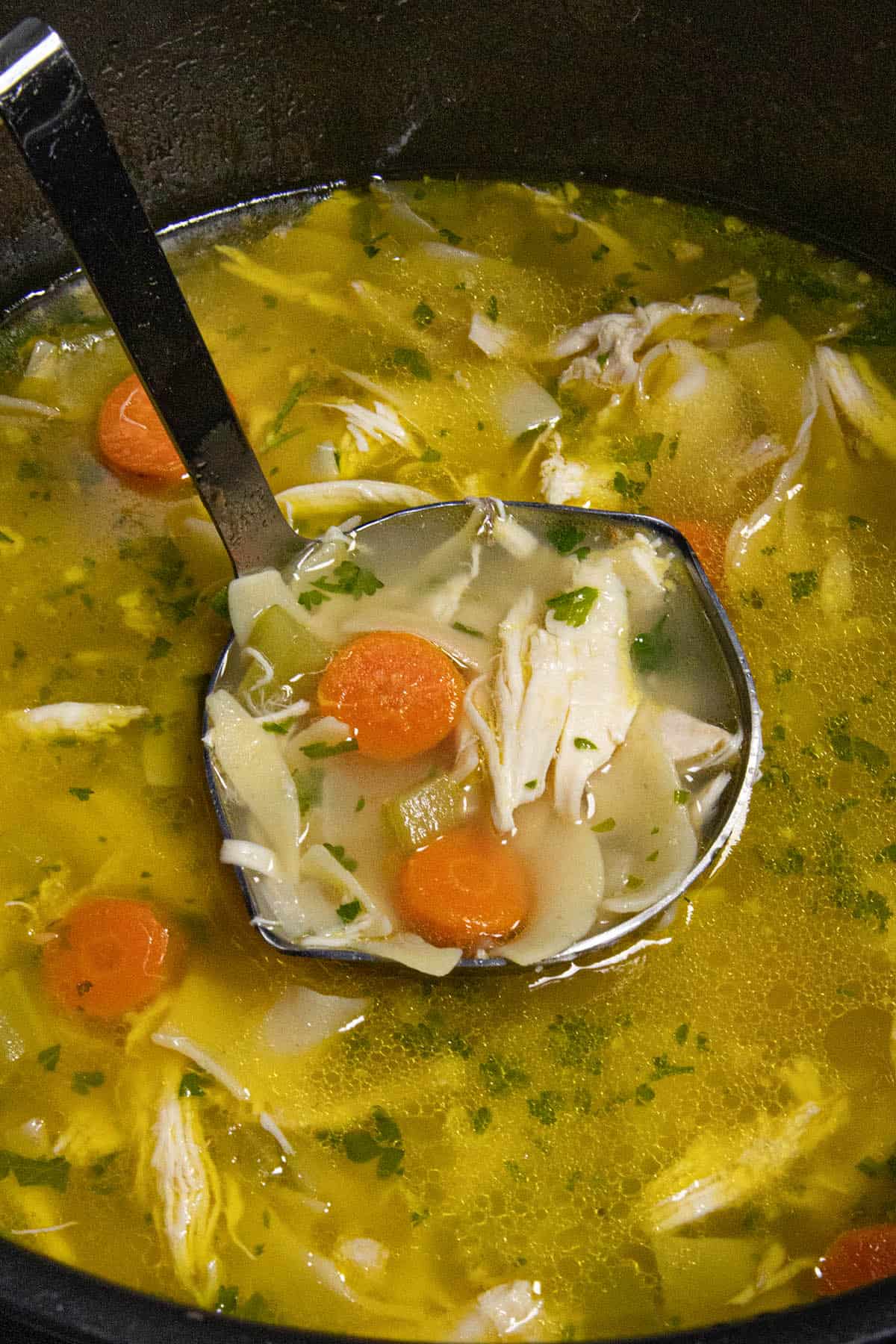 A ladle of Homemade Chicken Noodle Soup being scooped from the simmering pot