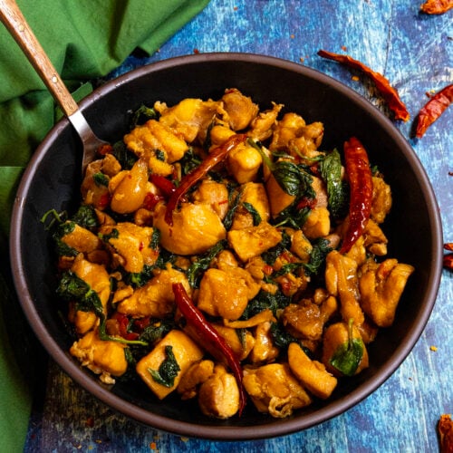 A bowl filled with saucy Three Cup Chicken (San Bei Ji), with lots of basil and hot chilies